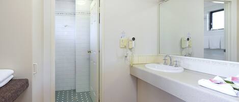 A bathroom with a white sink, a mirror, and a shower area.