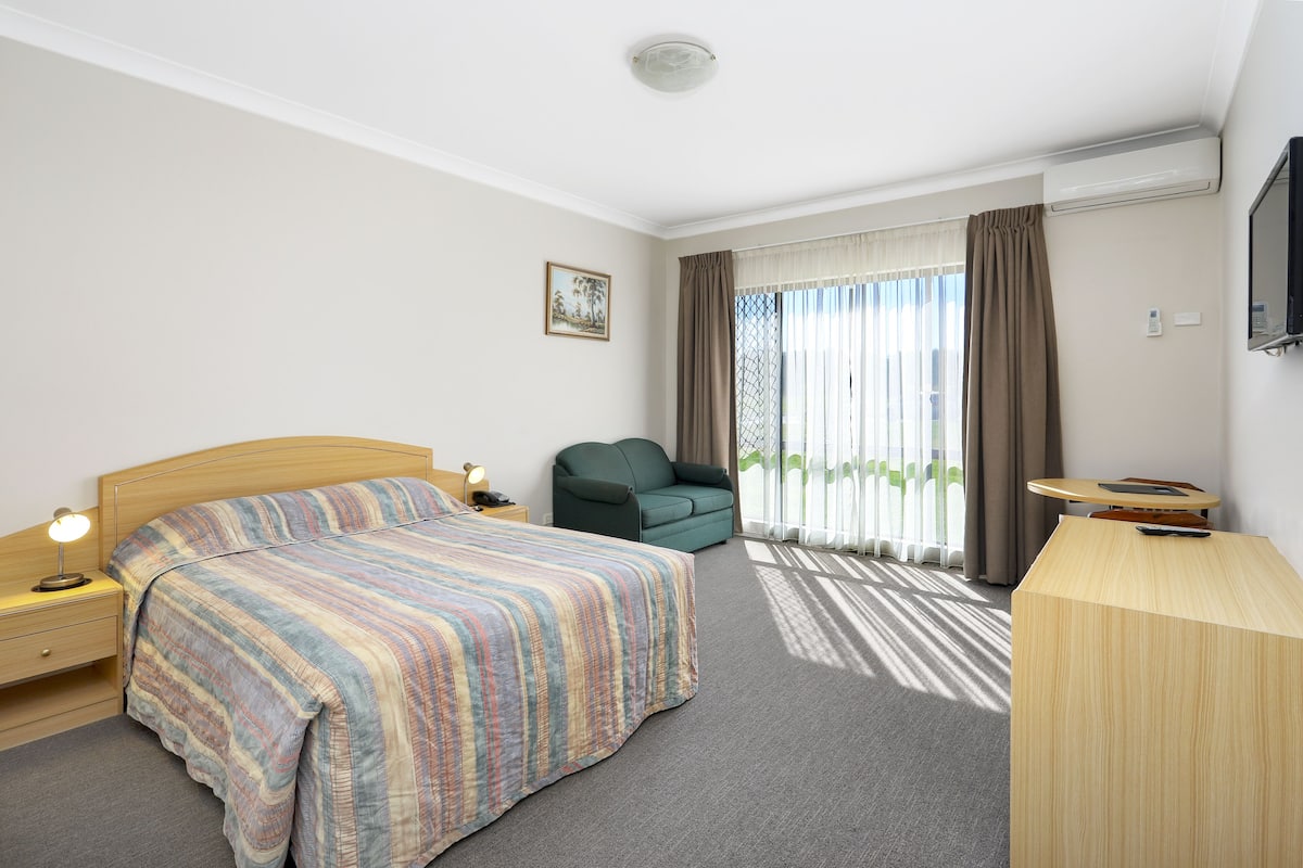A hotel room with a bed, a desk, a chair, a TV, and a window with curtains.