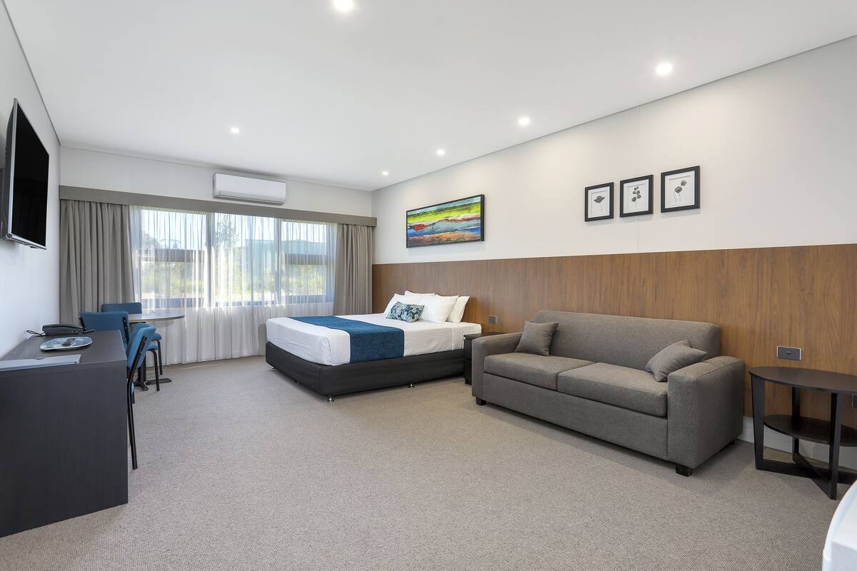 A modern hotel room with a bed, a sofa, a desk, and a TV.