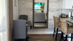 A modern kitchen with white cabinets, a dining area with wicker chairs, and a large mirror above the table.