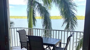 A balcony with a table and chairs, overlooking a body of water and palm trees.