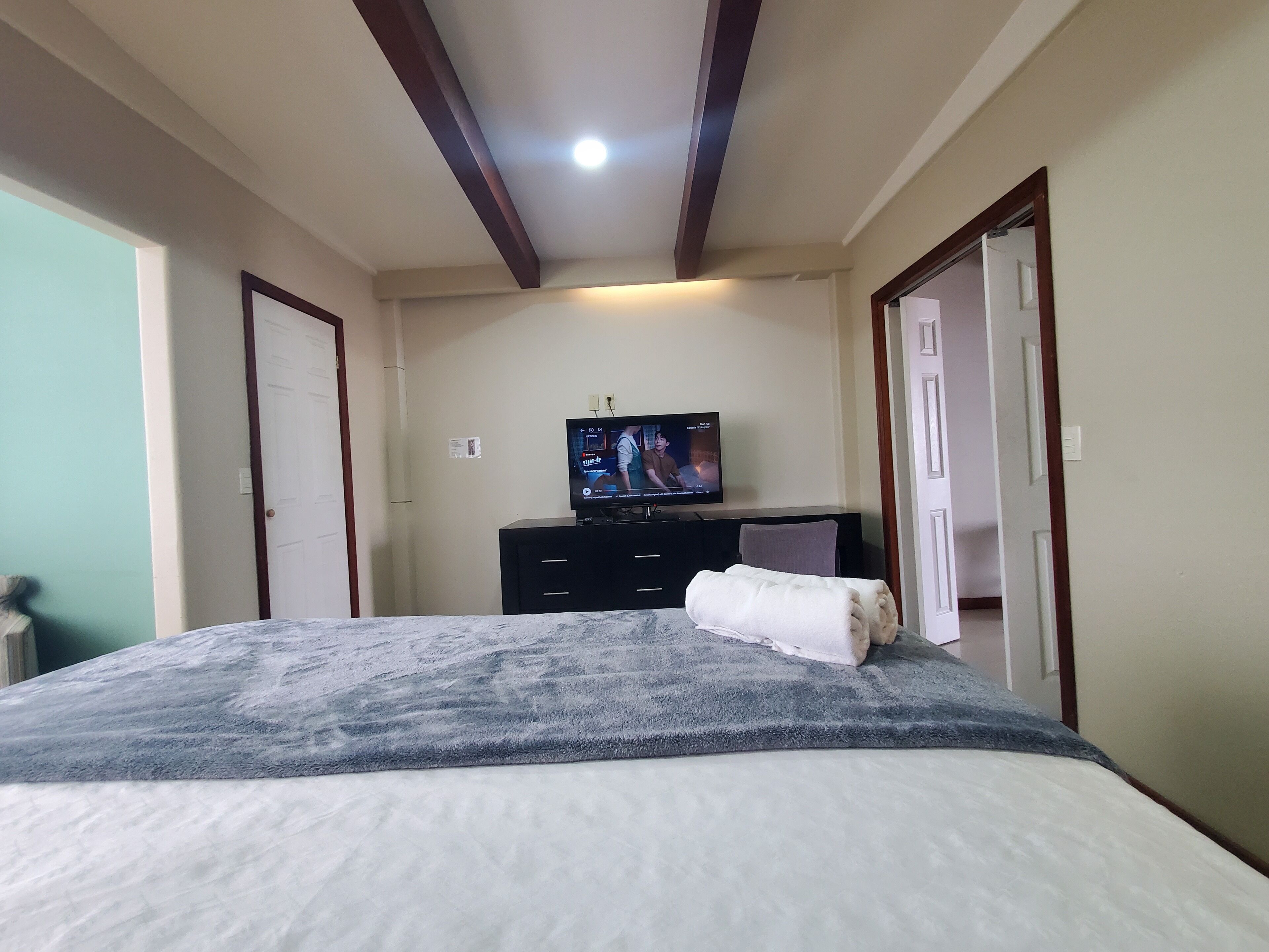 Ein Schlafzimmer mit einem Bett, einem Fernseher auf einer Kommode und einer Tür.