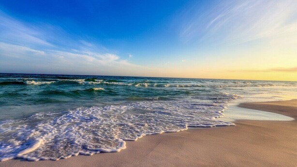 A beach with waves gently lapping onto the shore under a clear sky.