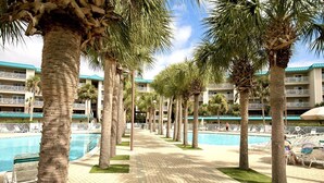 A hotel pool area with palm trees, lounge chairs, and a clear sky.