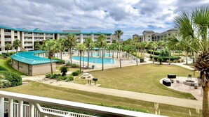 A resort with a swimming pool, palm trees, and a view of the hotel buildings.