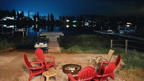 Un espacio con asientos junto al lago, con sillas rojas, un brasero y una mesa.