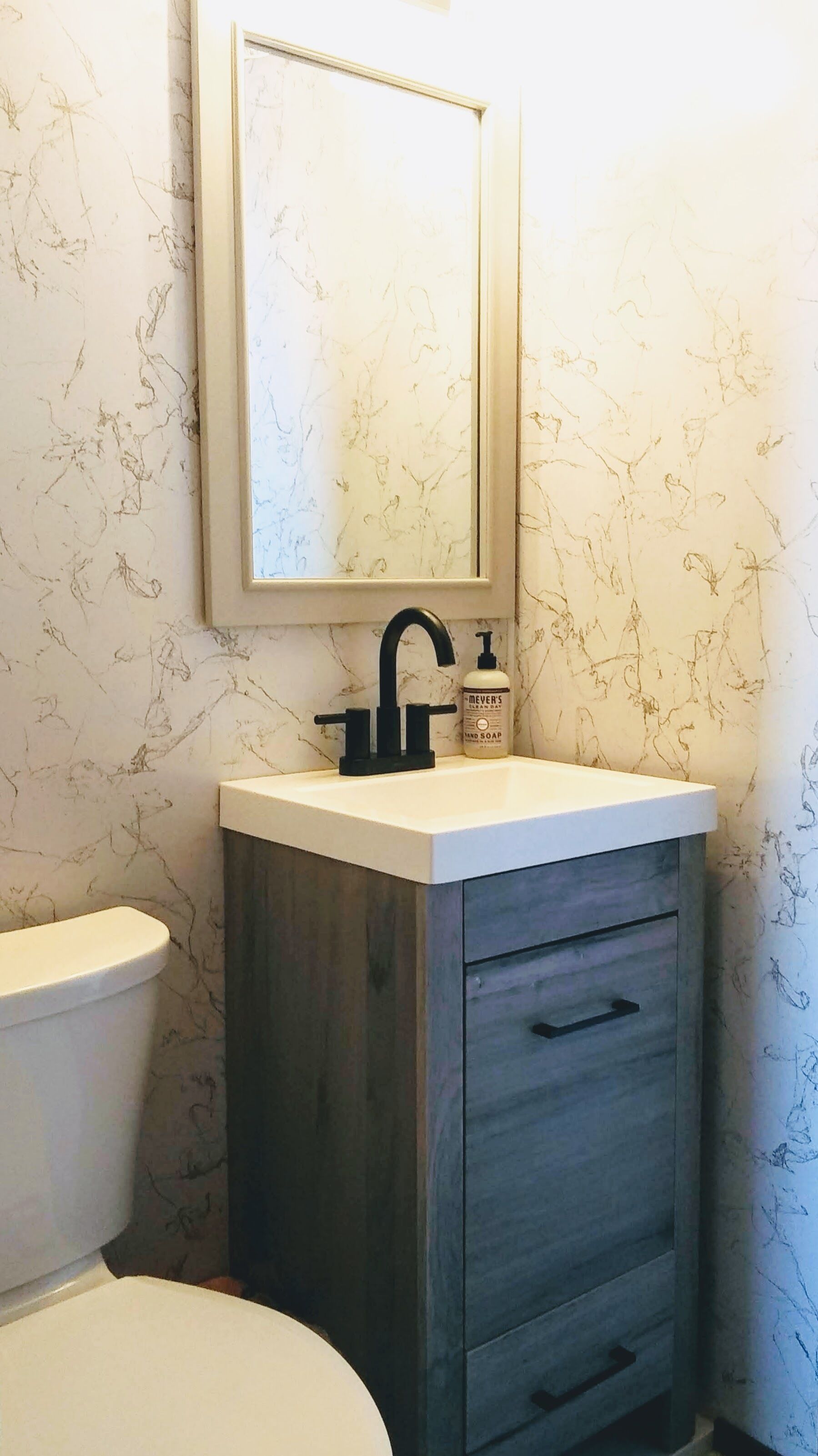 A bathroom with a white toilet, a dark wood cabinet with drawers, a black faucet, and a bottle of hand soap.