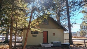 Una pequeña cabaña con puerta roja, un letrero que dice "Camp Rut-A-Muz" y una valla de madera que rodea la propiedad.