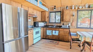 Una cocina compacta con armarios de madera, un refrigerador de acero inoxidable, un microondas y una estufa. Hay una ventana que ofrece luz natural y vistas al exterior.