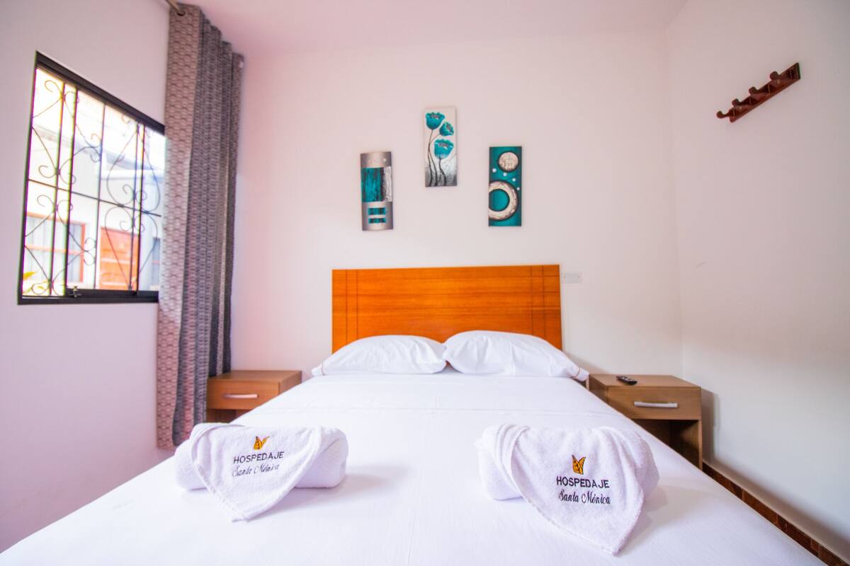 A hotel room with a wooden headboard, white bedding, two bedside tables, and artwork on the wall.