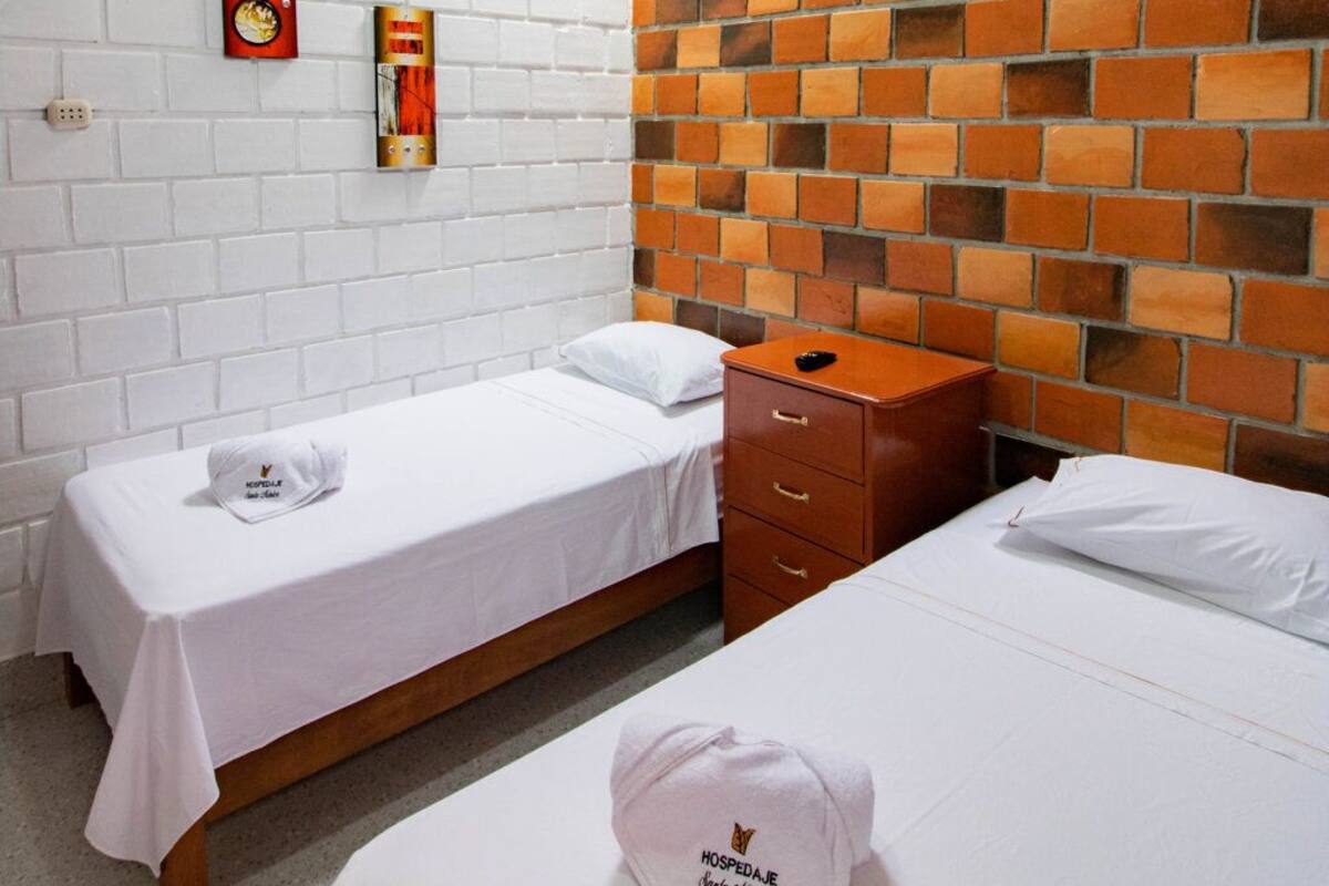 A hotel room with two single beds, a white brick wall, a wooden headboard, and a ceiling fan.