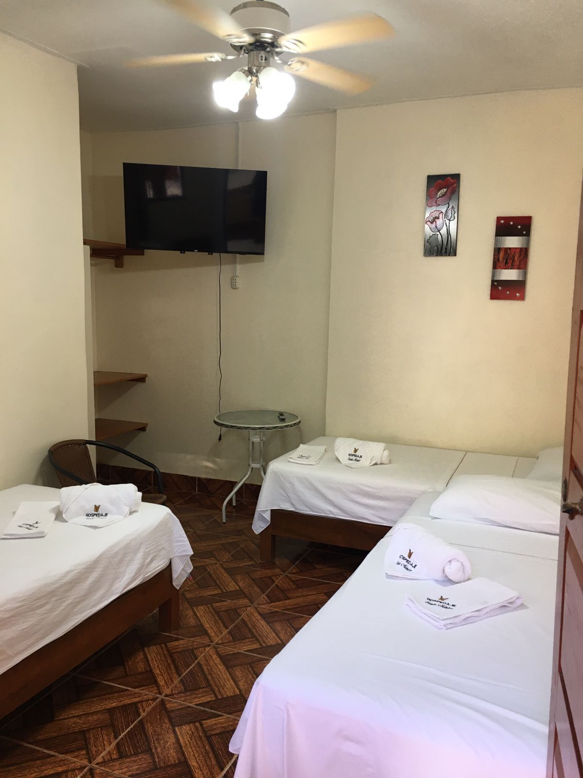 A hotel room with two beds, a ceiling fan, a TV mounted on the wall, and a small table.