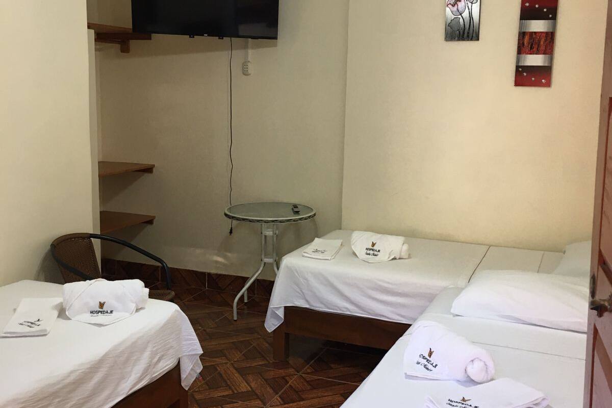 A hotel room with two beds, a ceiling fan, a TV mounted on the wall, and a small table.