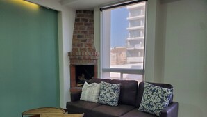 A living room with a brown leather sofa, patterned cushions, a small wooden table, and a brick fireplace. - Cozy apartment with a view (Tijuana)