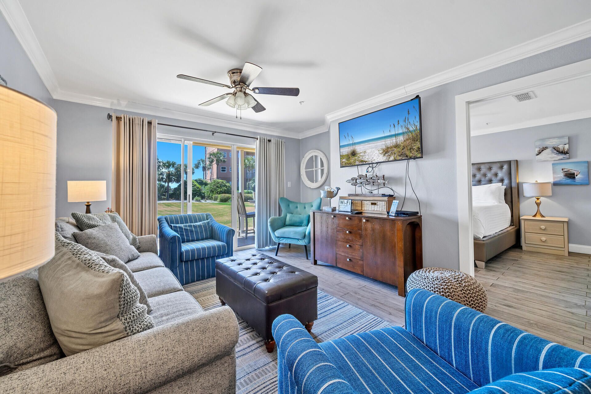 A spacious living room with a sofa, armchair, and ottoman, a wooden cabinet, and a ceiling fan.