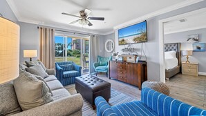 A spacious living room with a sofa, armchair, and ottoman, a wooden cabinet, and a ceiling fan. - Gulf Views! Ground Unit! Patio! Ciboney 1002! (Miramar Beach)