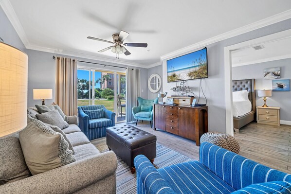 A spacious living room with a sofa, armchair, and ottoman, a wooden cabinet, and a ceiling fan. - Gulf Views! Ground Unit! Patio! Ciboney 1002! (Miramar Beach)