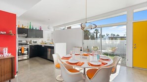 A modern kitchen with a dining area, featuring a large window and a bright yellow door. - Designer Wexler Oasis with Saltwater Pool & Spa (Palm Springs)