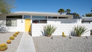 A modern house with a yellow door, white walls, and a gravel driveway. - Designer Wexler Oasis with Saltwater Pool & Spa (Palm Springs)