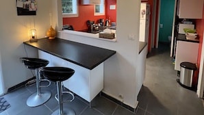 A compact kitchen with a black countertop, white cabinets, and two bar stools. - 032 - 3 *** villa in a quiet area close to the beaches and the city center (SOULAC SUR MER)