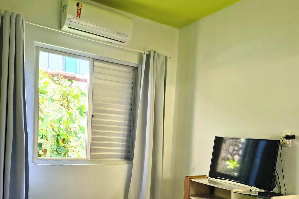 Ein Hotelzimmer mit Bett, Fernseher auf einem Schrank, Fenster mit Vorhängen und einer Wandklimaanlage.