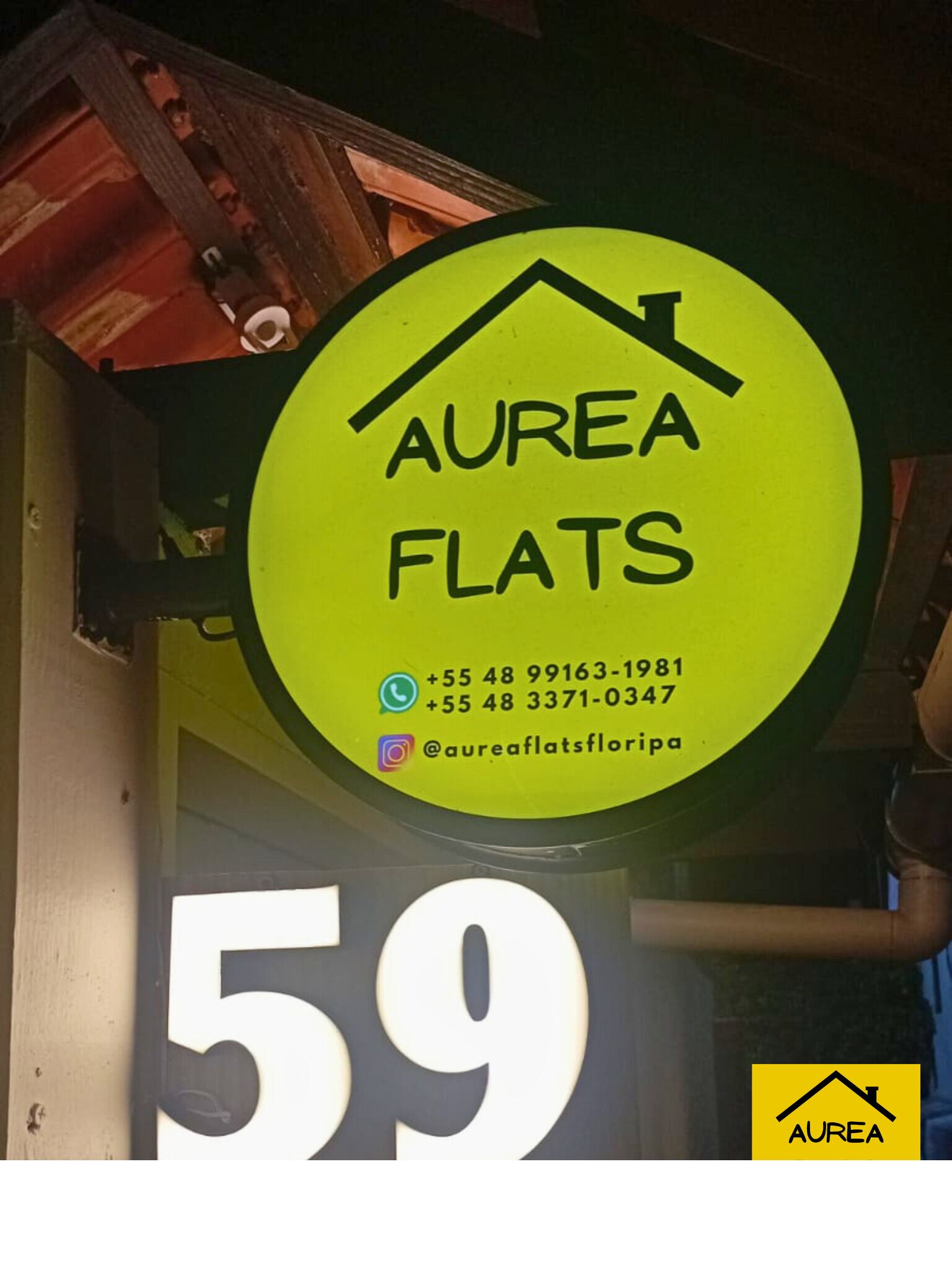 Un letrero amarillo con el texto "AUREA FLATS" y un icono de una casa, indicando un anuncio de bienes raíces.