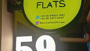 Un letrero amarillo con el texto "AUREA FLATS" y un icono de una casa, indicando un anuncio de bienes raíces.