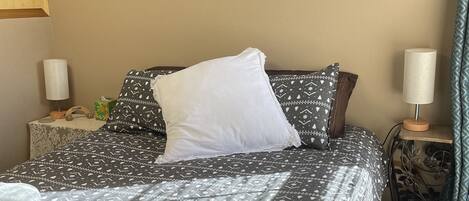 A neatly made bed with patterned bedding, a framed wall decoration of the moon phases, and bedside lamps.
