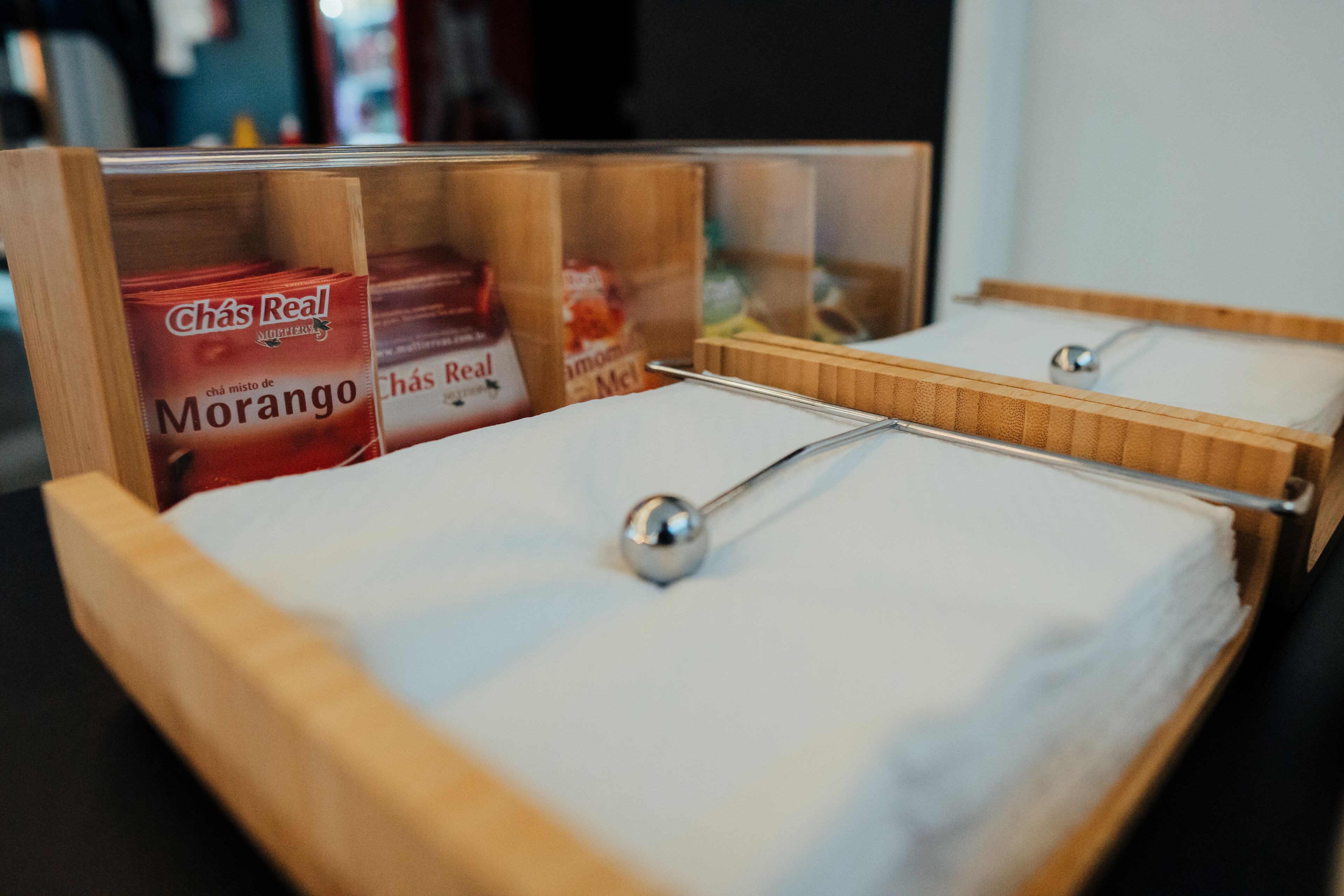 Habitación de hotel con cabeceros de madera, estructura de cama metálica y un minibar con Chás Real Morango y barras de chocolate Chás Real.