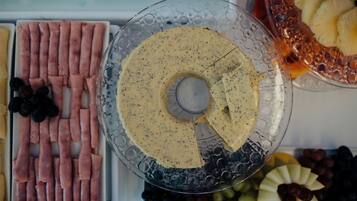 A glass platter with a creamy spread, surrounded by various fruits and sliced meats.