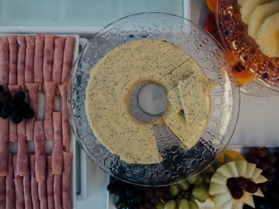 A glass platter with a creamy spread, surrounded by various fruits and sliced meats.