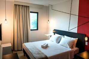 A hotel room with a bed, a TV, a window with curtains, and a wall with a geometric design.