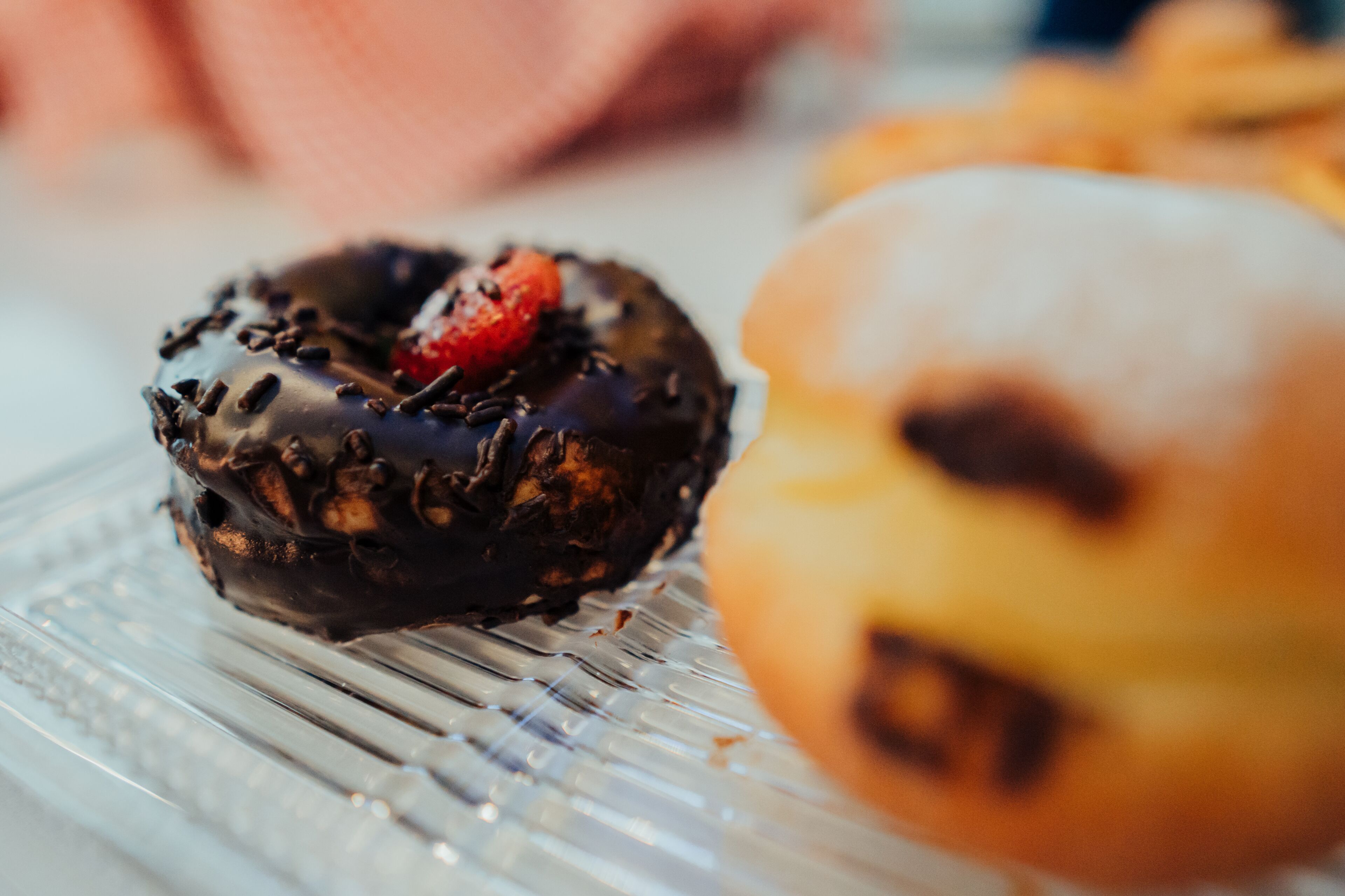 Primer plano de un donut cubierto de chocolate con una fresa sobre un plato de vidrio.