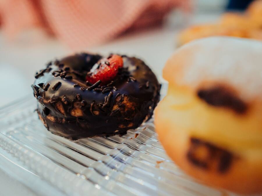 Primer plano de un donut cubierto de chocolate con una fresa sobre un plato de vidrio.