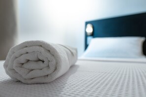 A neatly rolled white towel on a textured white bedspread in a hotel room.