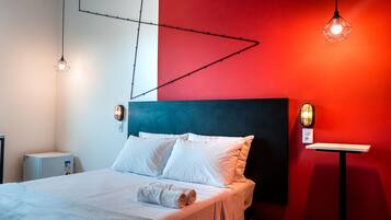 Una habitación de hotel moderna con cama, ropa de cama blanca, una pared de acento roja e iluminación colgante.