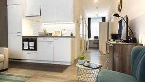 Une cuisine moderne avec des meubles blancs, un coin repas agrémenté d’une chaise bleue et une petite table d’appoint avec une plante.