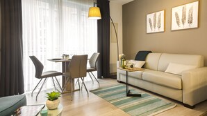 Un salon moderne avec un canapé, une table à manger et des chaises, une lampe et des œuvres d’art accrochées au mur.