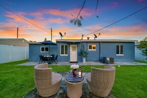 Un jardin à l’arrière d’une maison d’habitation, avec un patio, du mobilier d’extérieur et une maison à la façade bleue.
