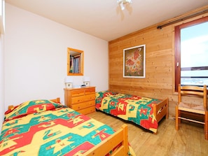 A bedroom with two beds, a wooden dresser, a mirror, and a window with a view.
