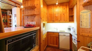 Una cocina compacta con armarios de madera, horno integrado, lavavajillas y una pequeña encimera.