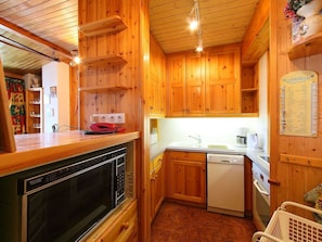 A compact kitchen with wooden cabinets, a Sharp microwave, a red telephone, and a white dishwasher.
