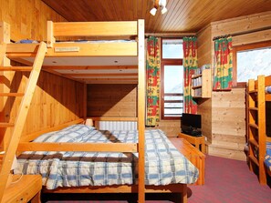 A wooden cabin with bunk beds, a television, and a window with curtains.