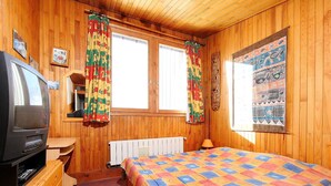 Una habitación con paneles de madera, una cama, un televisor y un ventanal con cortinas.
