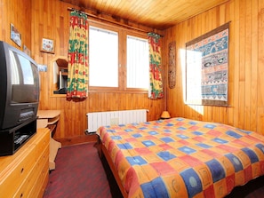 Ein Zimmer mit Holzwandverkleidung, einem Bett, einem Fernseher und einem Fenster mit Vorhängen.