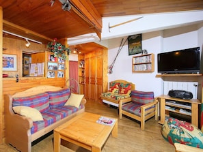 A cozy cabin interior with a wooden ceiling, a sofa, a chair, a coffee table, and a bookshelf.