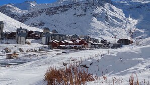 Un pueblo nevado en la montaña con edificios, incluyendo un hotel con techo rojo, y telesillas al fondo.