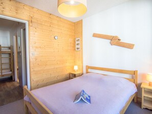 Puupaneloitu huone, jossa on sänky, yöpöytä, lamppu ja puinen hylly.