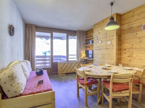 Tunnelmallinen huone, jossa on puuseinä, ruokapöytä tuoleineen, kuviollinen päällinen sisältävä sohva ja suuri ikkuna, jossa on verhot.