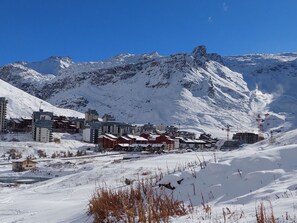 A snow-covered mountain town with buildings, including a hotel with a red roof, and ski lifts in the background.